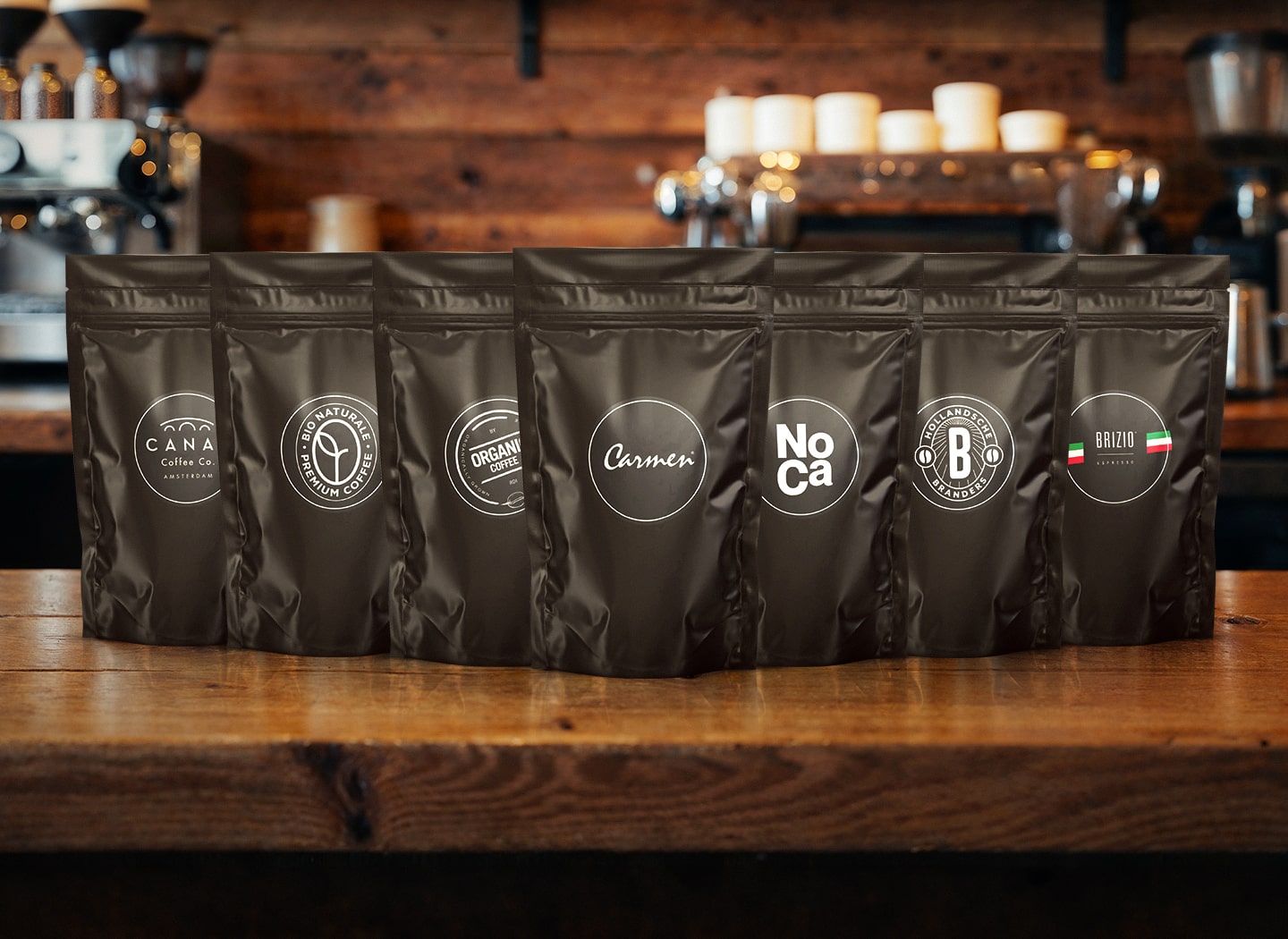 Zwarte samplezakjes van CaféHuis met verschillende koffiemerken, opgesteld op een houten bar in een gezellige koffiezaak