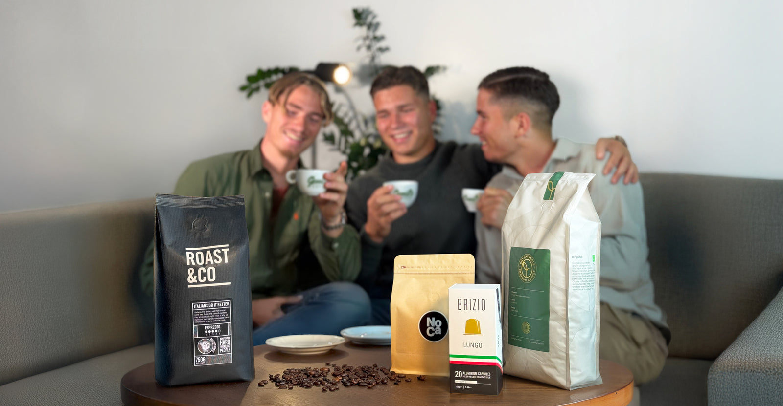 Drie vrienden drinken koffie op een bank met koffiebonen en zakken op een tafel op de voorgrond
